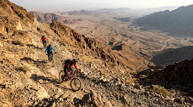 Mountain bikers descending rocky trail above Hatta valley at dawn